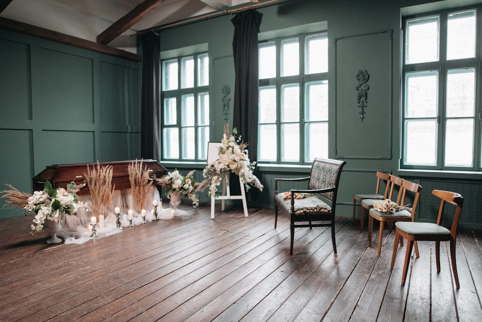 A floral arrangement scene in a room with wooden flooring and green-paneled walls. The arrangement includes white flowers such as roses and lilies, complemented by tall, beige pampas grass, all displa