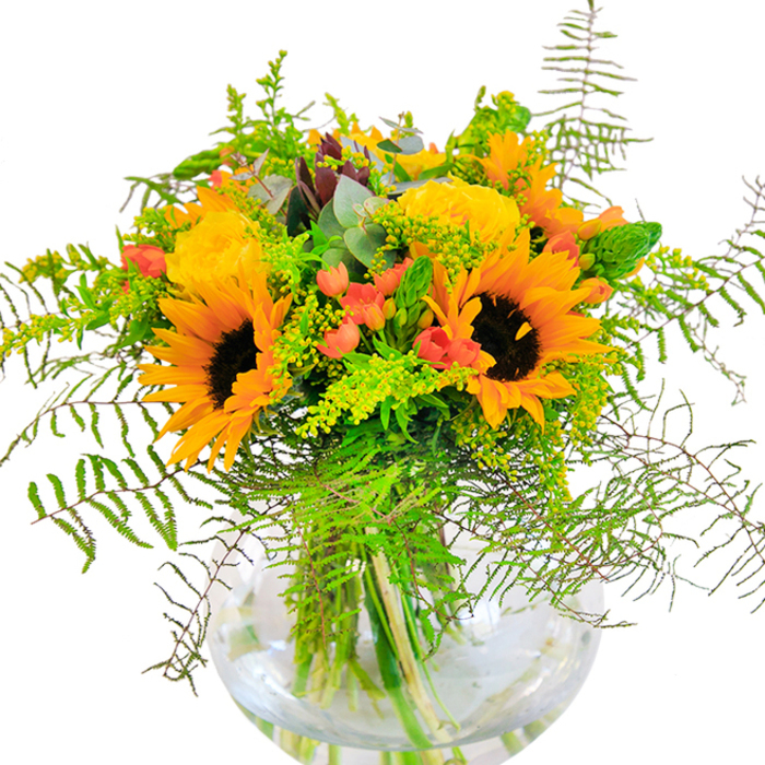 First impressions of this Wembley bouquet evoke pure, sun-drenched exuberance-an arrangement alive with the joyful interplay of yellow, orange, and green, as seen at the height of summer in local gardens or along Olympic Way. Sunflowers with large, open faces and rich brown centers stand at the core, their unfurling petals shining alongside opulent yellow roses tightly coiled in elegant spirals. Between these, clusters of vivid red Hypericum berries glisten, their round gleam offering a spirited burst against the softly textured backdrop of ferns and other greenery. Airy filler flowers, possibly solidago boasting delicate yellow tips, intermingle with slender spikes of green and the soft, blue-toned eucalyptus, bringing depth and a gentle woodland accent. Held together in a clear, spherical vase-echoing modern styling and showcasing the arrangement's architectural grace-the vivid stems remain visible beneath the water, adding a sense of freshness and authenticity. Gentle light playing across the bouquet enhances every contrast, from velvety sunflower discs to crisp, cool greens. The scent hovers subtly between rose and earth, conjuring memories of open-air gatherings and summer strolls near Fryent Country Park. Whether presented as a centerpiece for special milestones or as a thoughtful gesture, this bouquet radiates with the optimism and careful artistry synonymous with Wimbledon's expert florists.